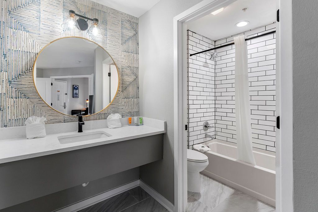 Modern bathroom vanity with round mirror and adjacent glass shower with patterned tile walls