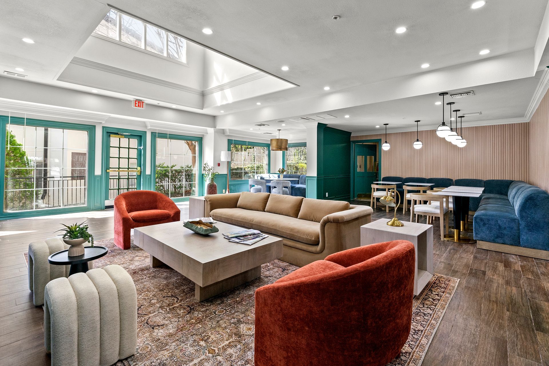 Bright modern lounge with sofas, red chairs, dining area, and large windows under skylights