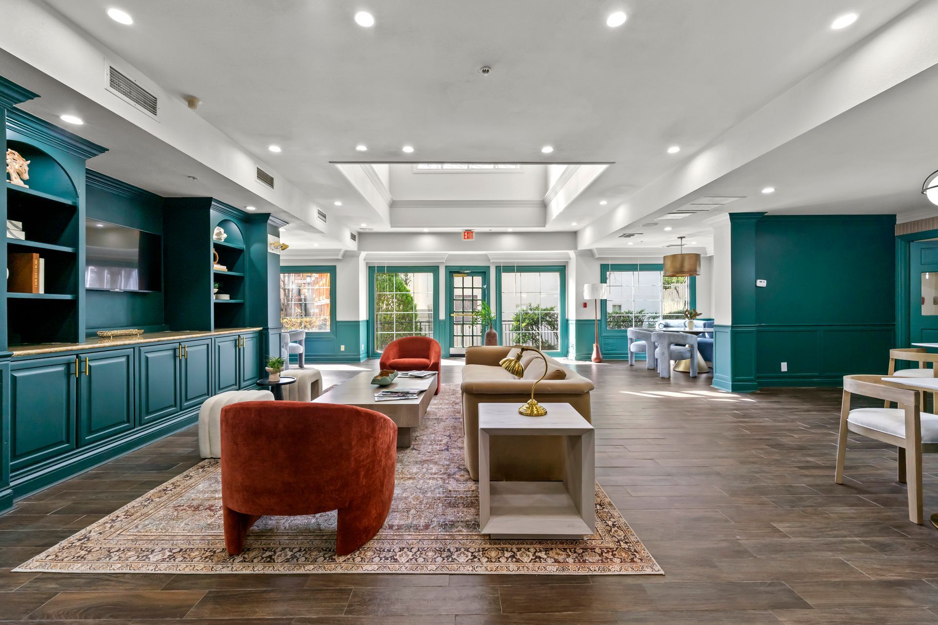 Bright modern living room with teal built-ins, wood floors, and red chairs around a central coffee table