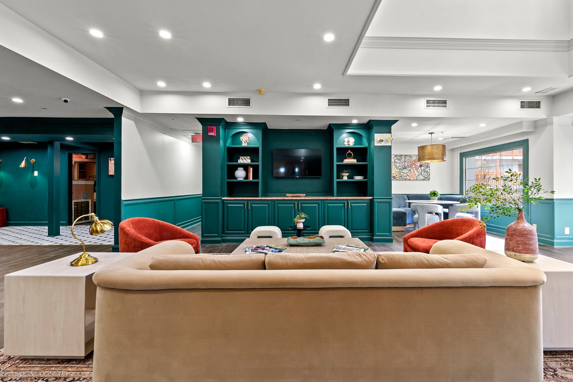 Modern living room with beige sofa, teal built-ins, orange chairs, and large windows