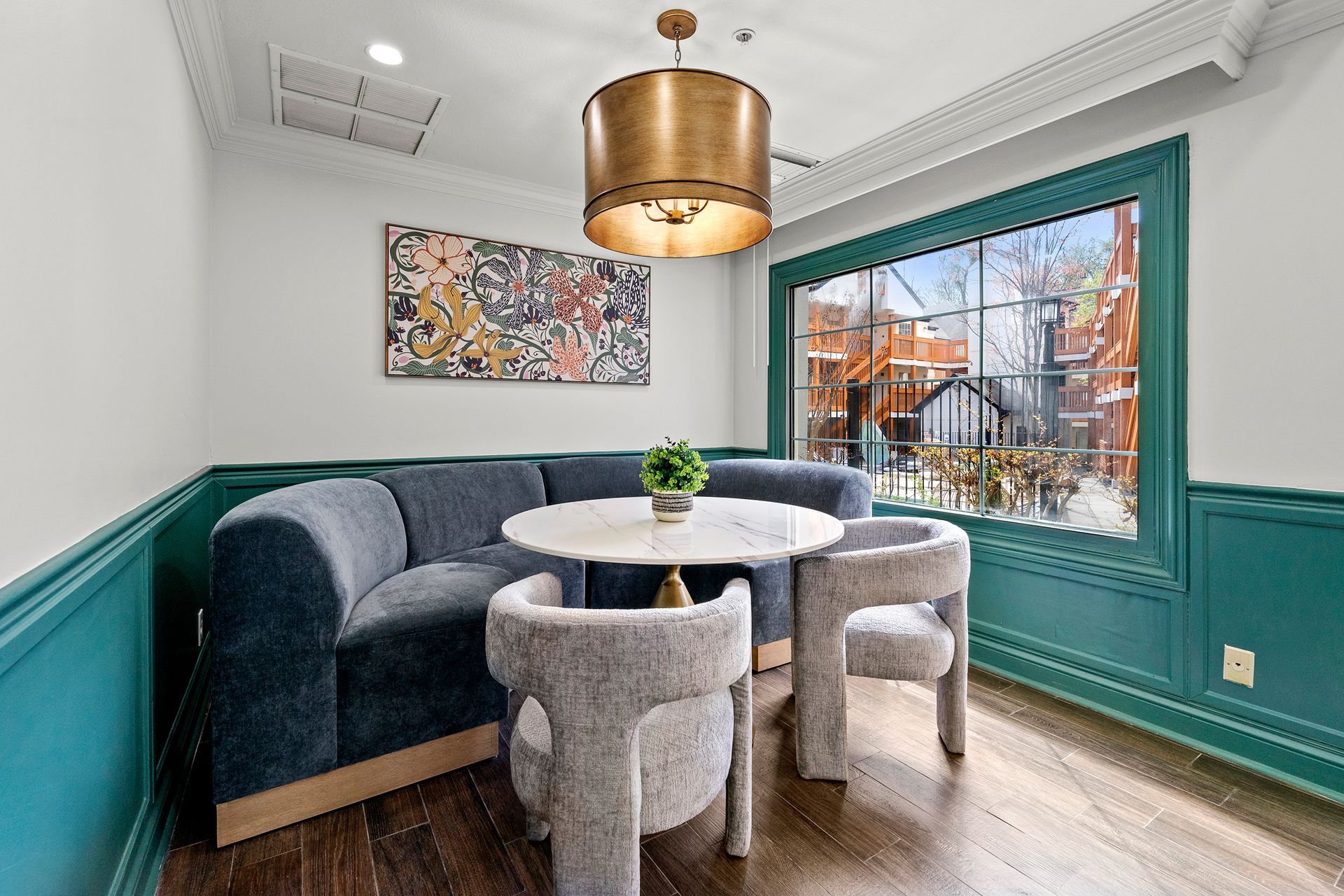 Small teal-trimmed seating nook with gray chairs, round table, pendant light, and window view outside