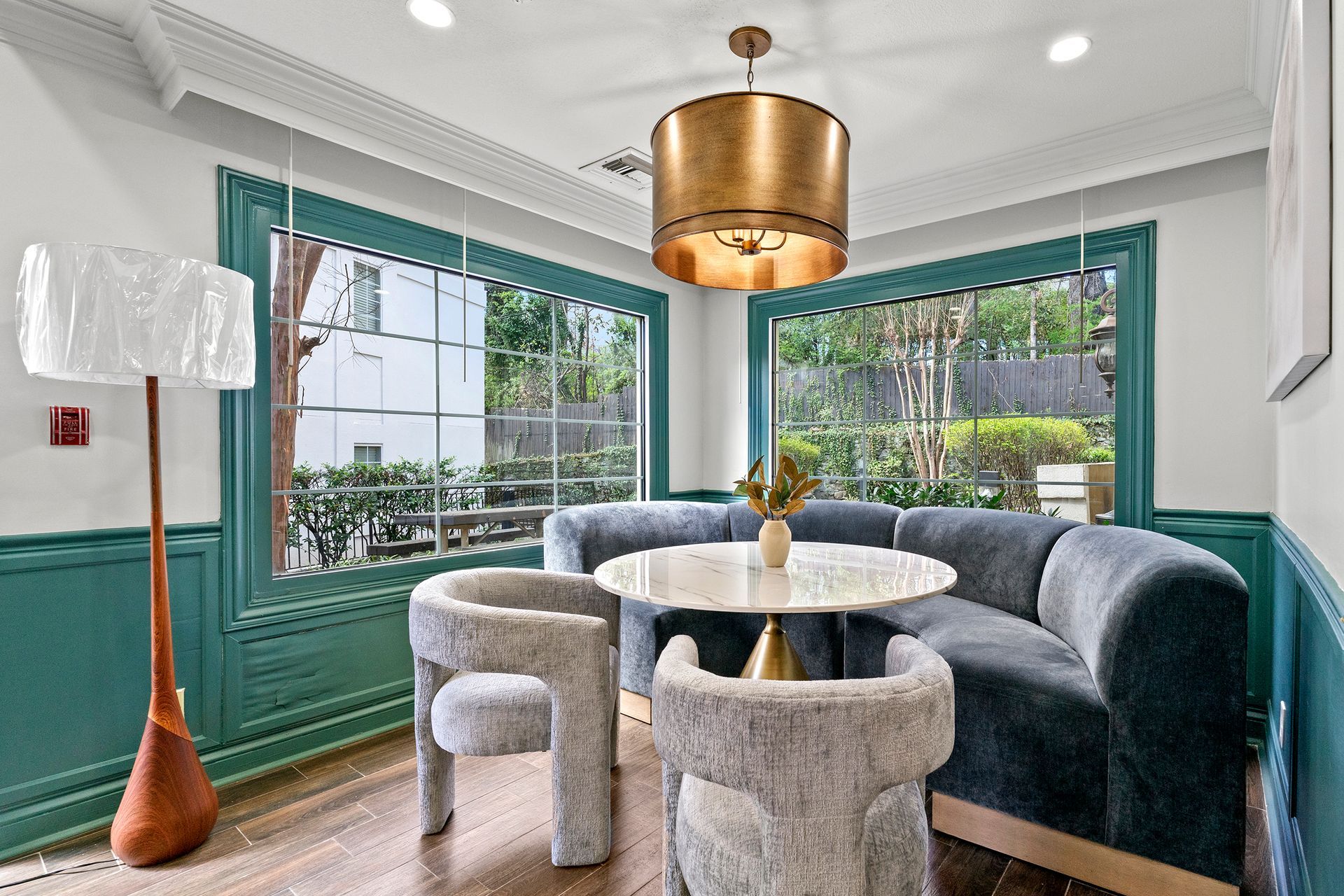 Bright dining nook with teal bay window seating, round table, gray chairs, and brass pendant light