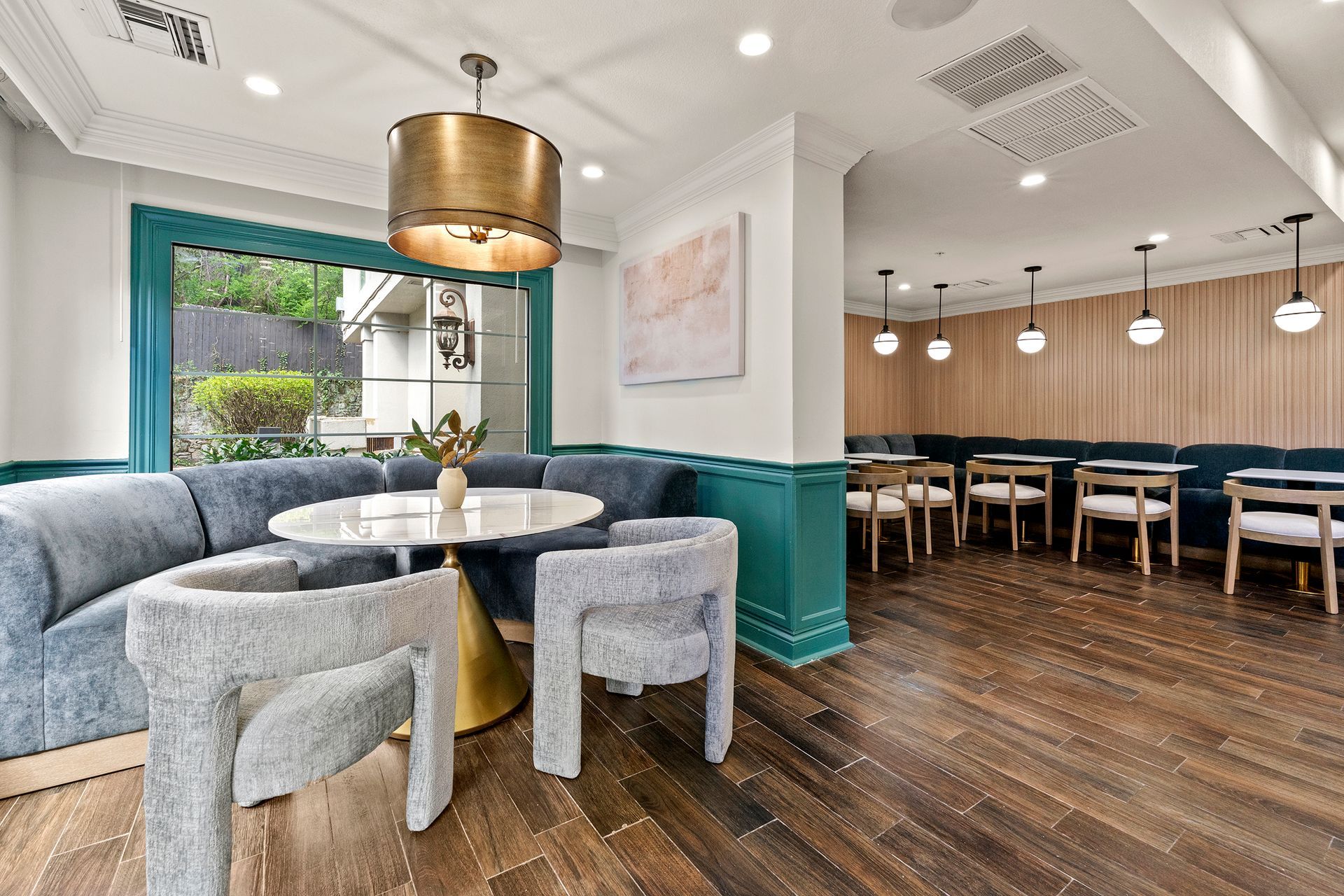 Cozy café seating with blue banquettes, round table, pendant lights, and wood floors adjacent to a dining area
