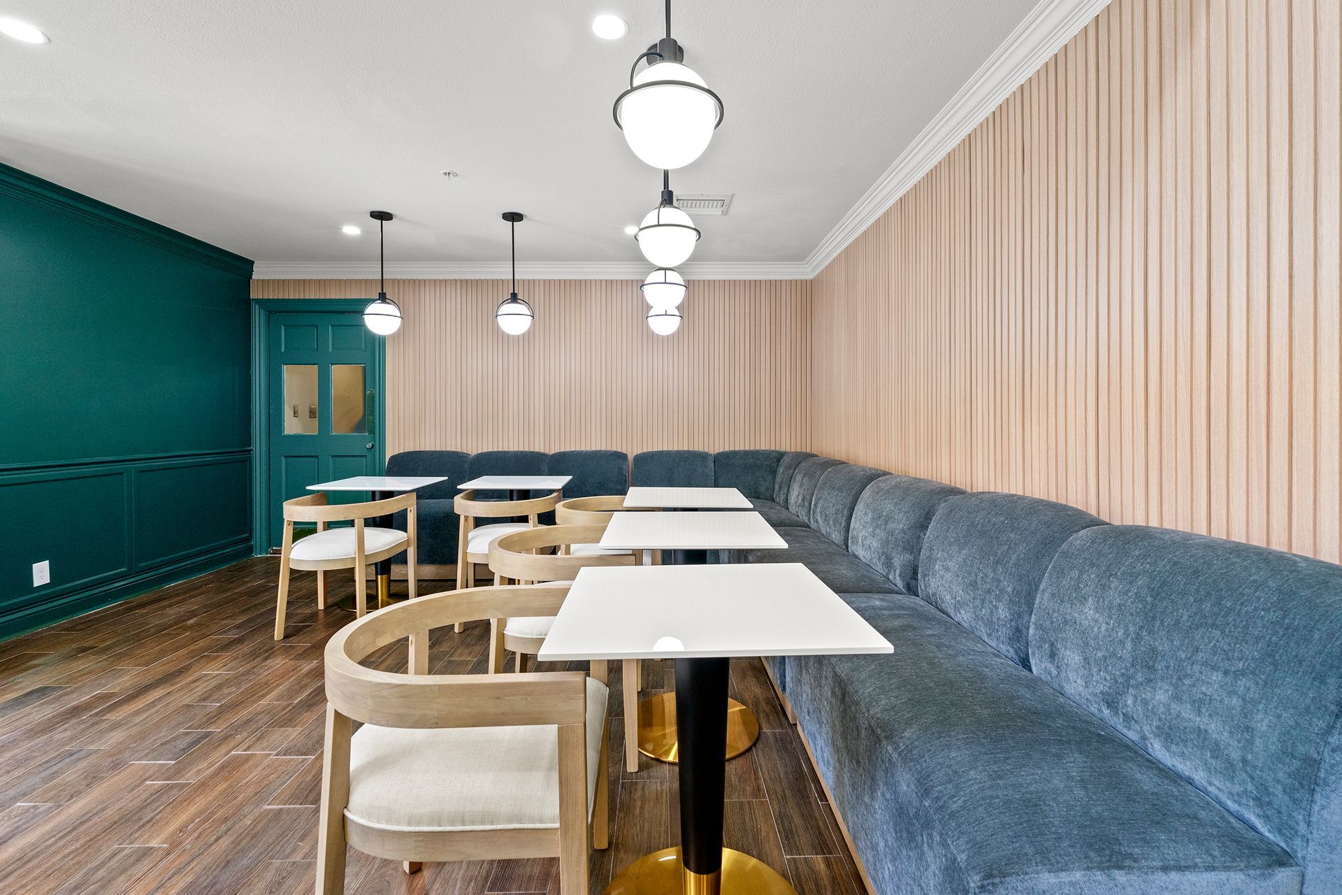 Modern café seating with white tables, blue banquette, teal wall, and wood-paneled interior