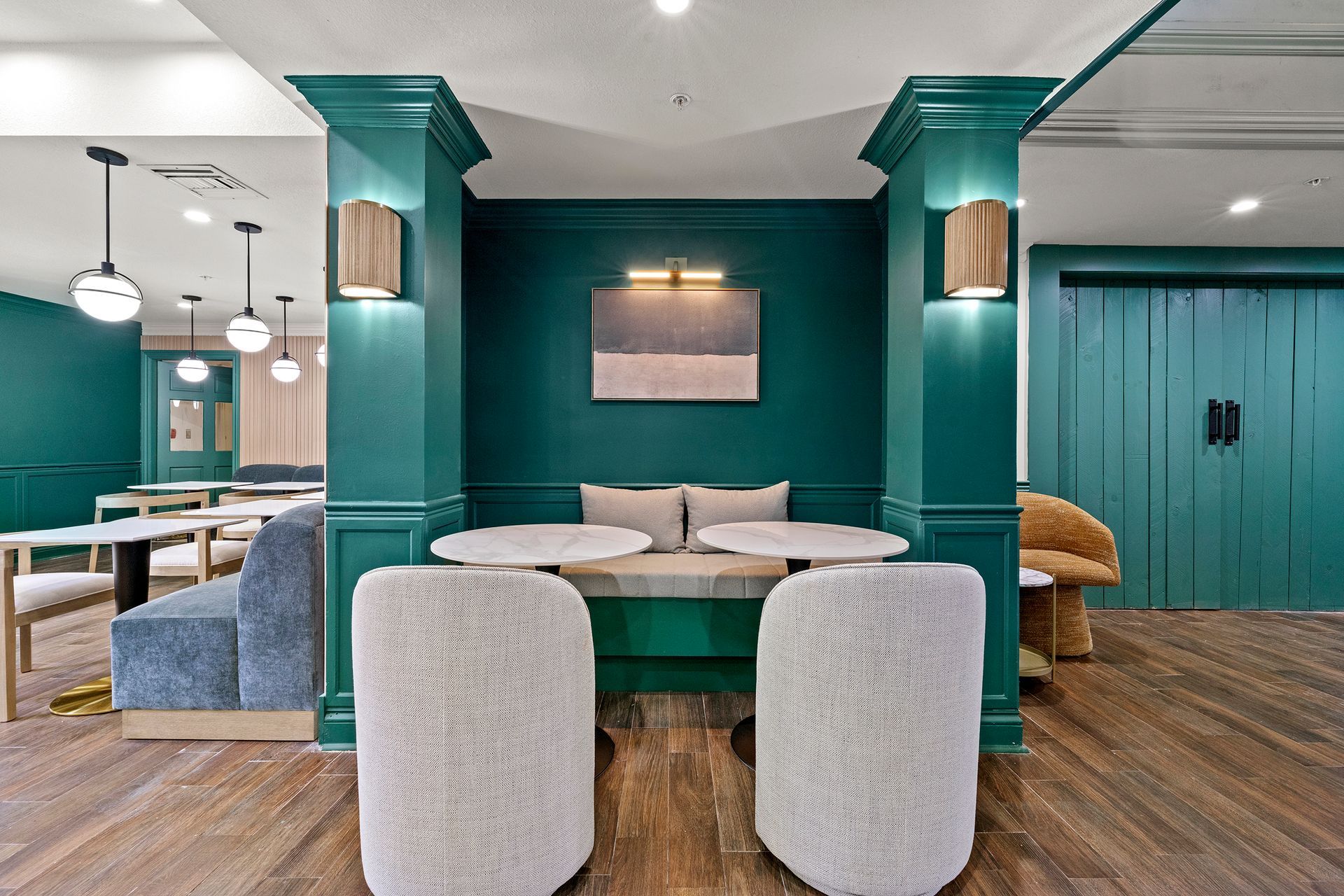 Teal lounge with round table, upholstered chairs, pendant lights, and wood flooring