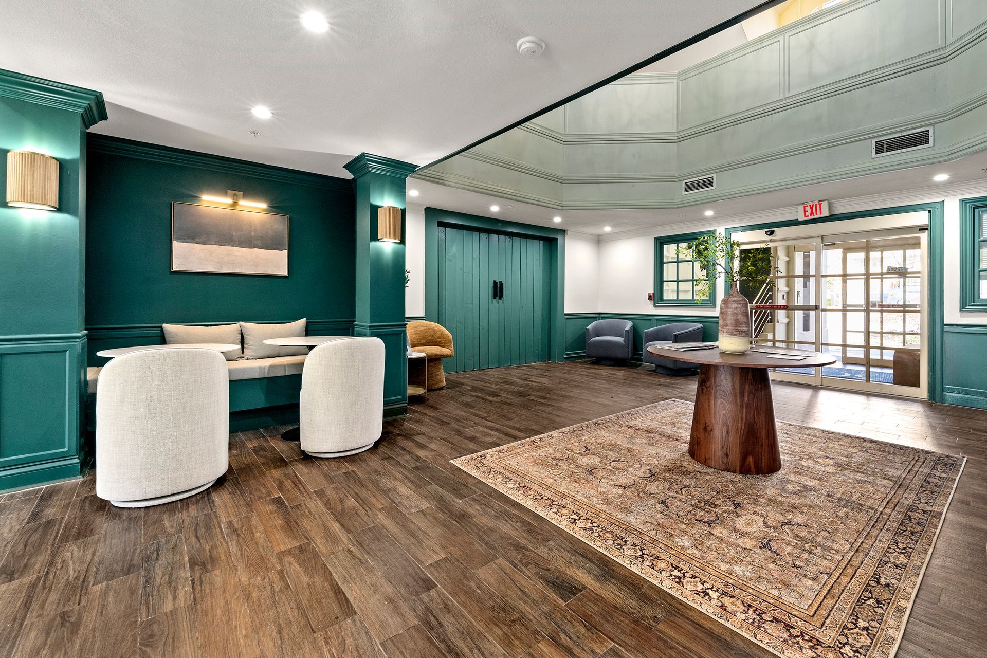 Empty modern lobby with teal walls, wood floors, seating, rug, and glass entrance doors