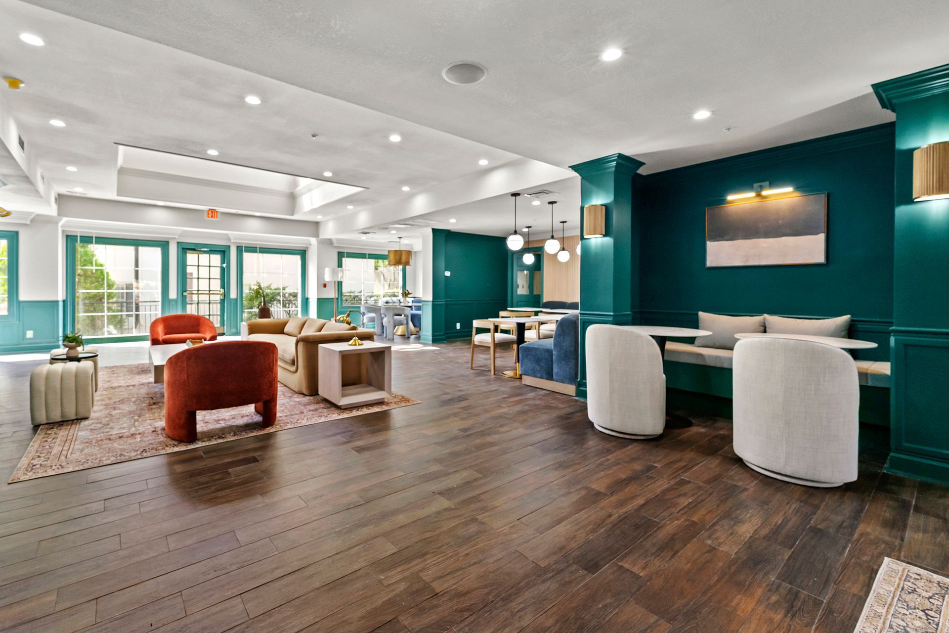Modern lounge with teal walls, wood floors, colorful chairs, and large windows letting in natural light