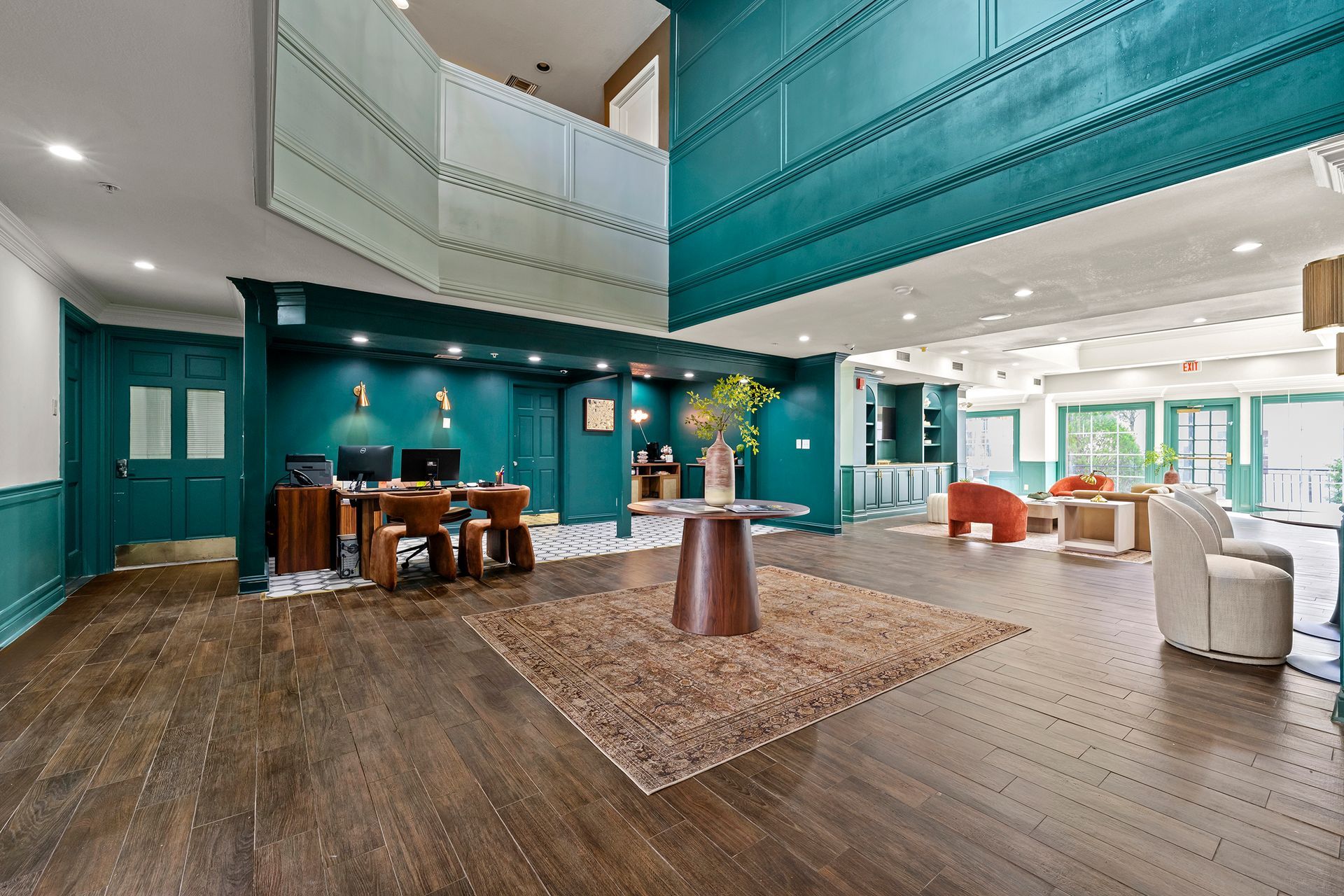 Spacious teal-and-white lobby with wood floors, seating, and a large open mezzanine.