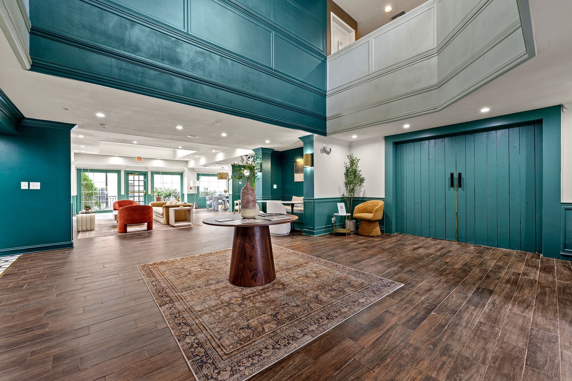 Spacious hotel lobby with teal walls, wood floors, lounge seating, and large double doors