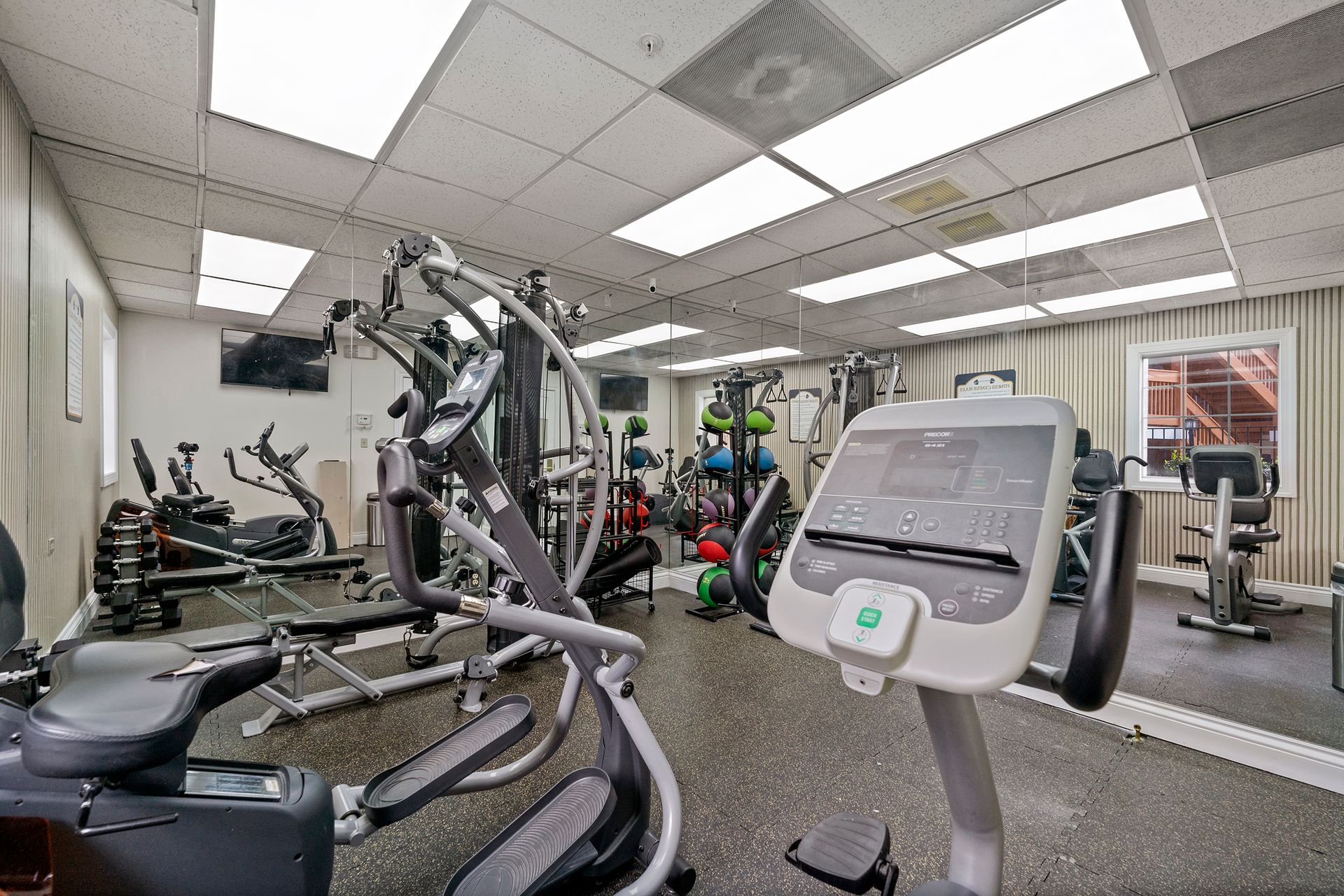 Gym with cardio and weight machines, mirrors, and bright ceiling lights
