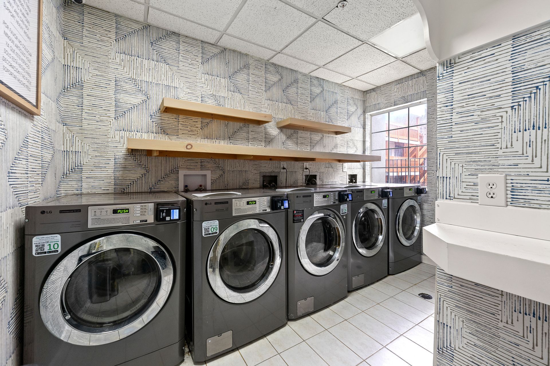 Laundry room with several front-loading washers lined along the wall and shelves above.