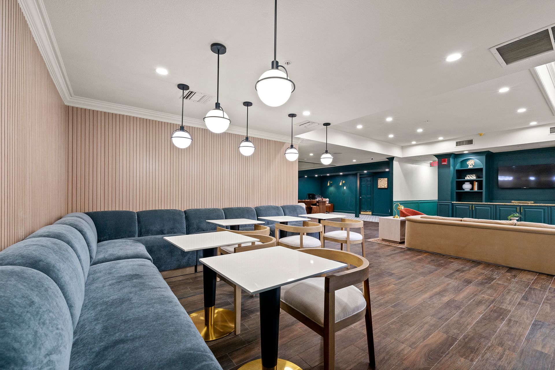 Modern lounge with blue seating, pendant lights, wood floors, and a teal reception counter