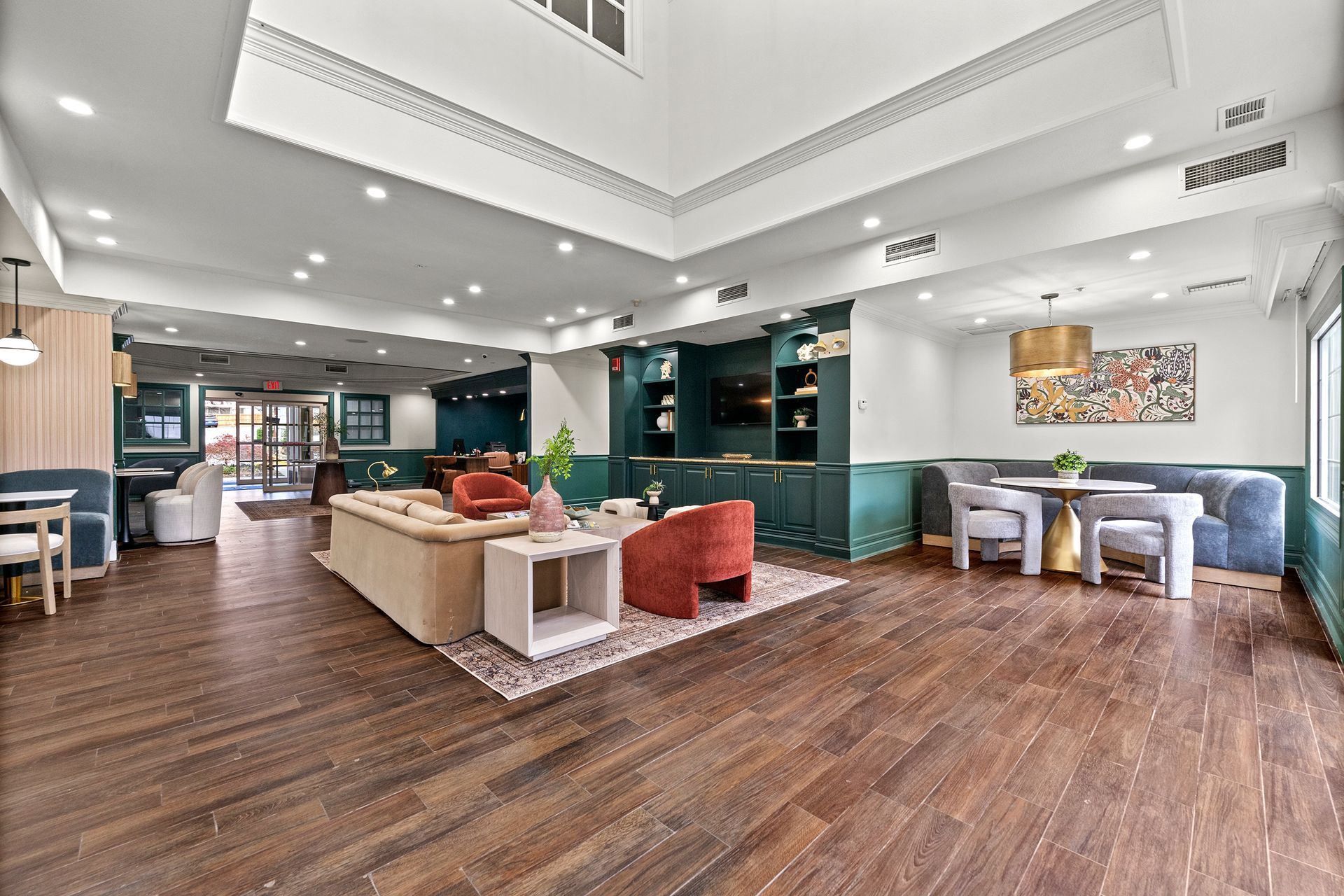 Spacious modern lounge with wood floors, teal seating, and a central sofa under bright ceiling lights