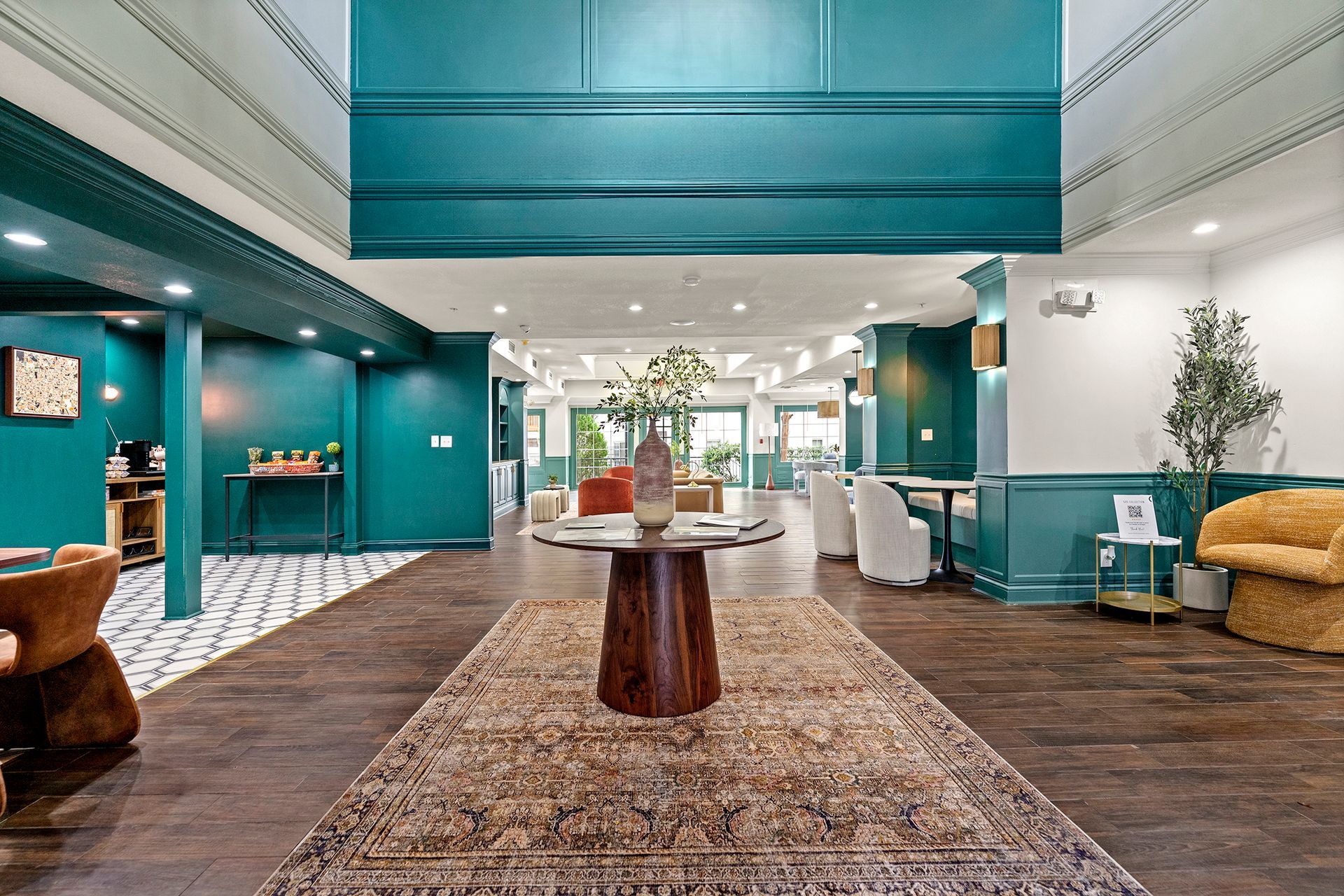 Modern hotel lobby with teal walls, central table, patterned rug, and seating areas