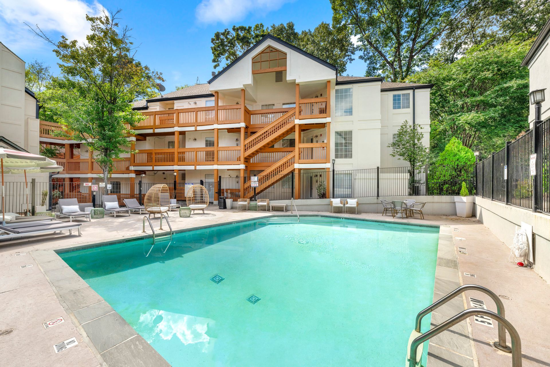Apartment complex pool with turquoise water, lounge chairs, and wooden balconies under trees