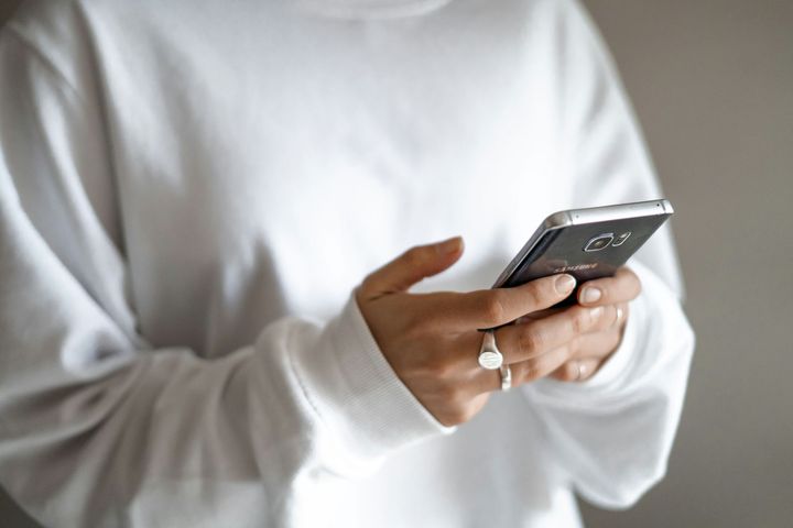 Person in a white sweater holding a smartphone and typing with both hands.