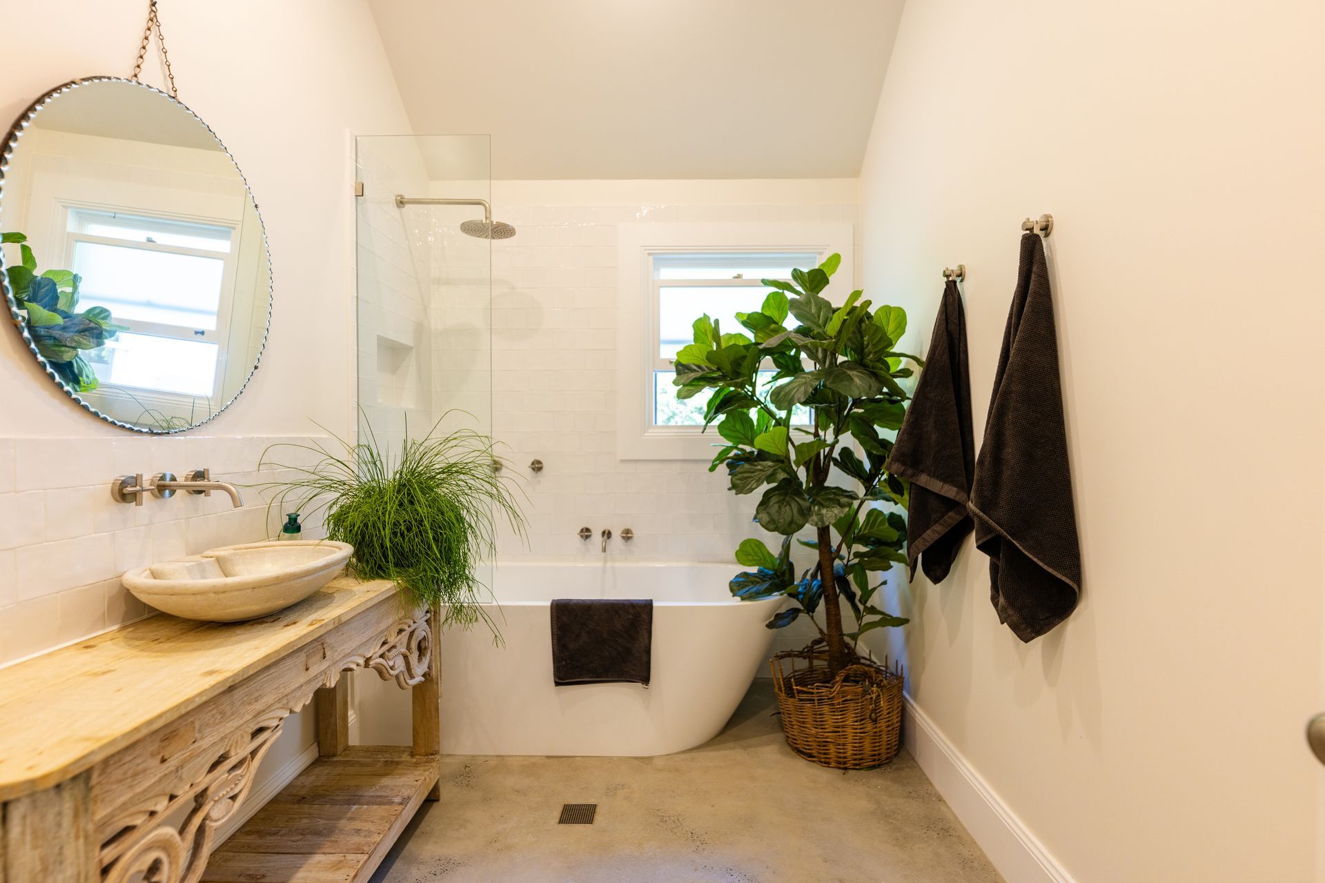 Bathroom with a round mirror, wooden vanity, soaking tub, and potted plant; neutral tones — Stark Building & Constructions In Berry, NSW