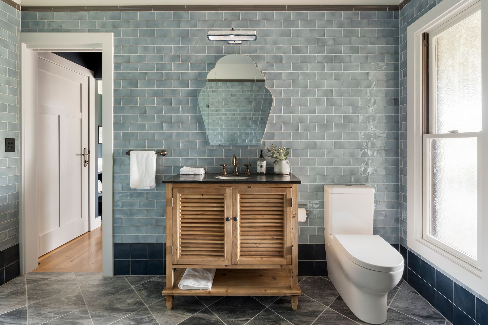 Bathroom with blue tile walls, wooden vanity, white toilet, and an open doorway — Stark Building & Constructions In Nowra, NSW