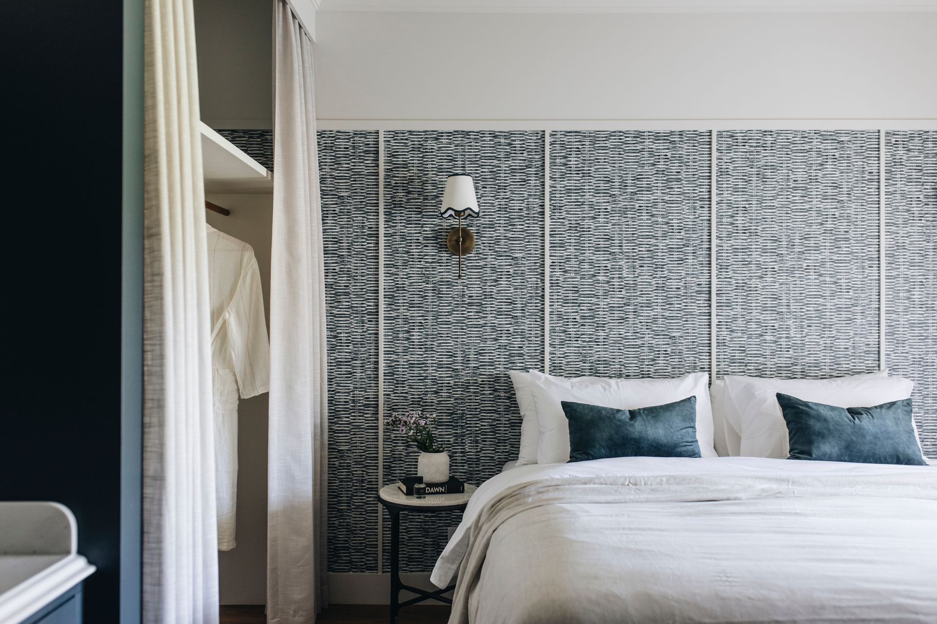 Bedroom with white bedding, blue pillows, patterned wall, and a robe in the closet — Stark Building & Constructions In Nowra, NSW