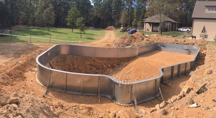 A metal swimming pool frame installed in a dirt excavation on a residential construction site.