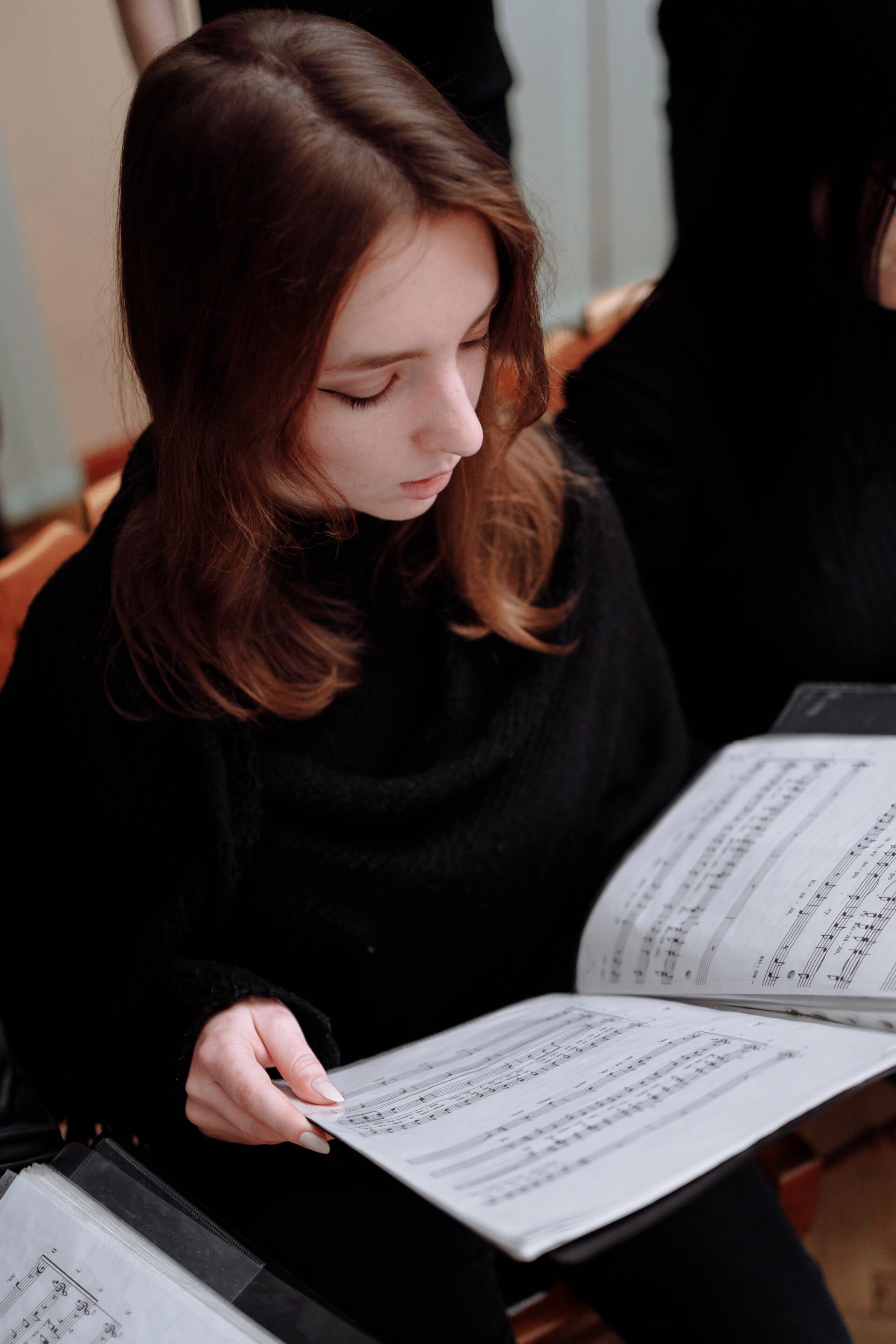 a woman in a black sweater is sitting in a chair reading sheet music .