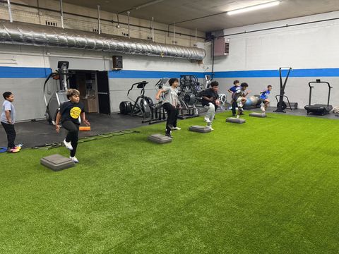People exercising in an indoor gym on turf, stepping on low platforms near stationary bikes.