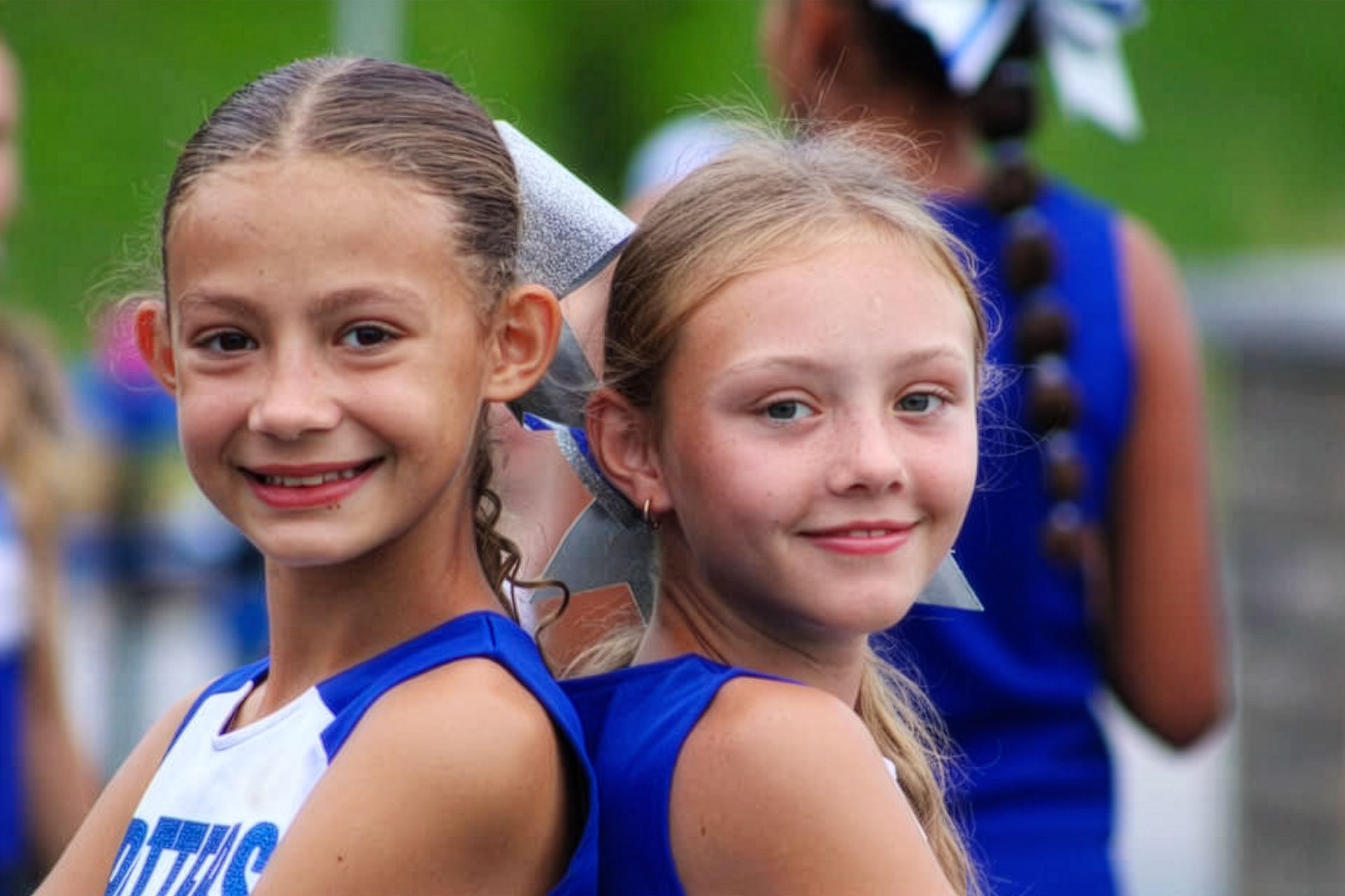 Two smiling girls in blue sports uniforms standing outdoors at a track event