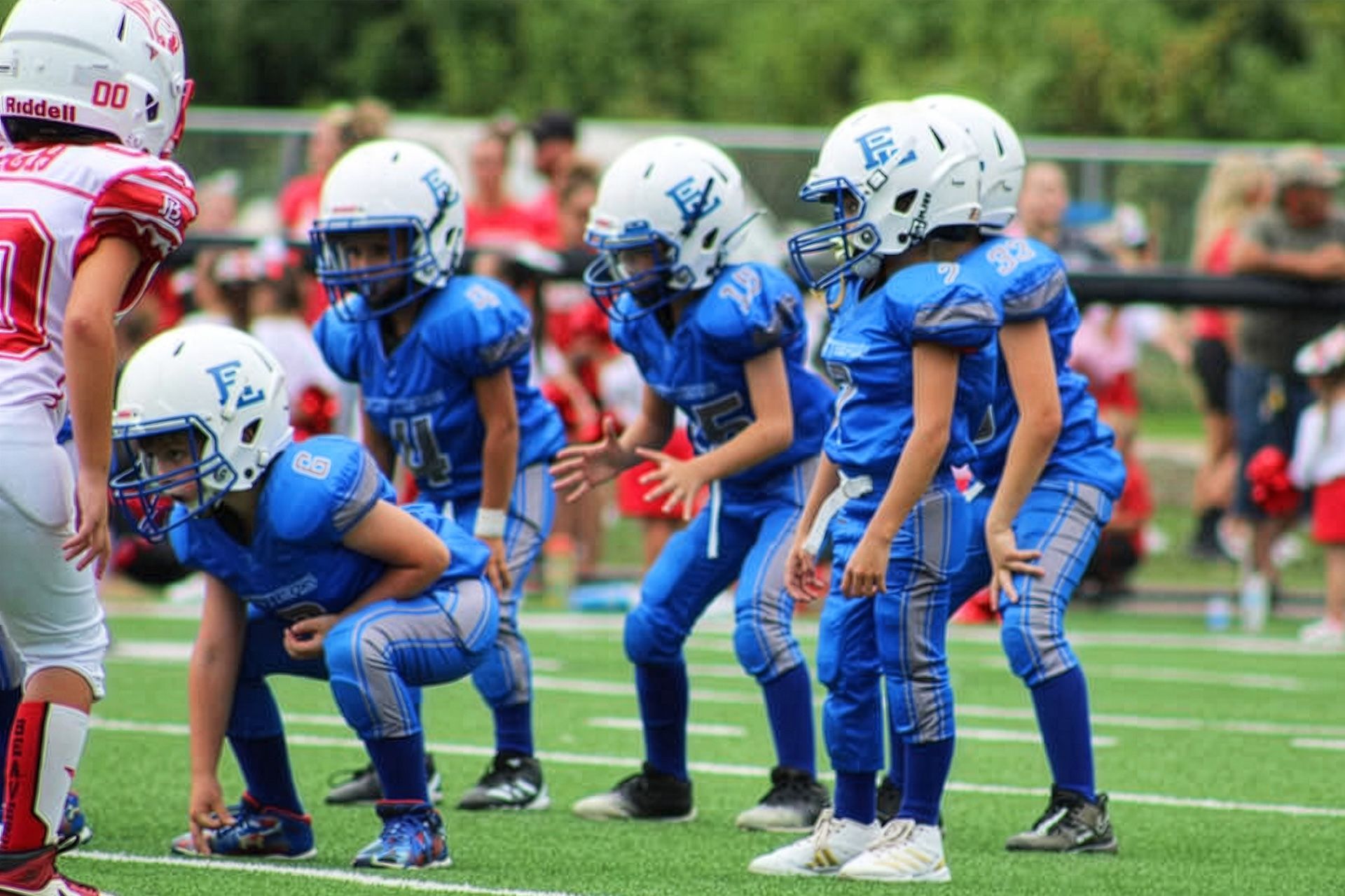 Youth football players in blue uniforms lined up at the line of scrimmage on a field