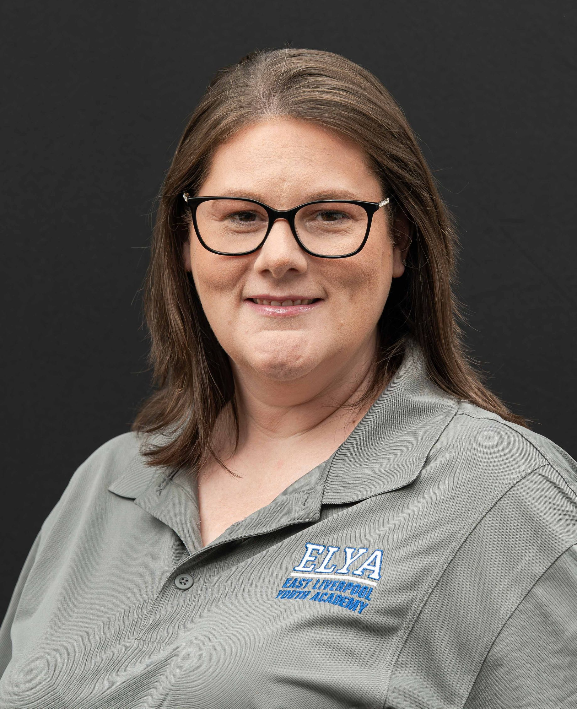 Portrait of a Amanda  in glasses and a gray shirt against a dark background.
