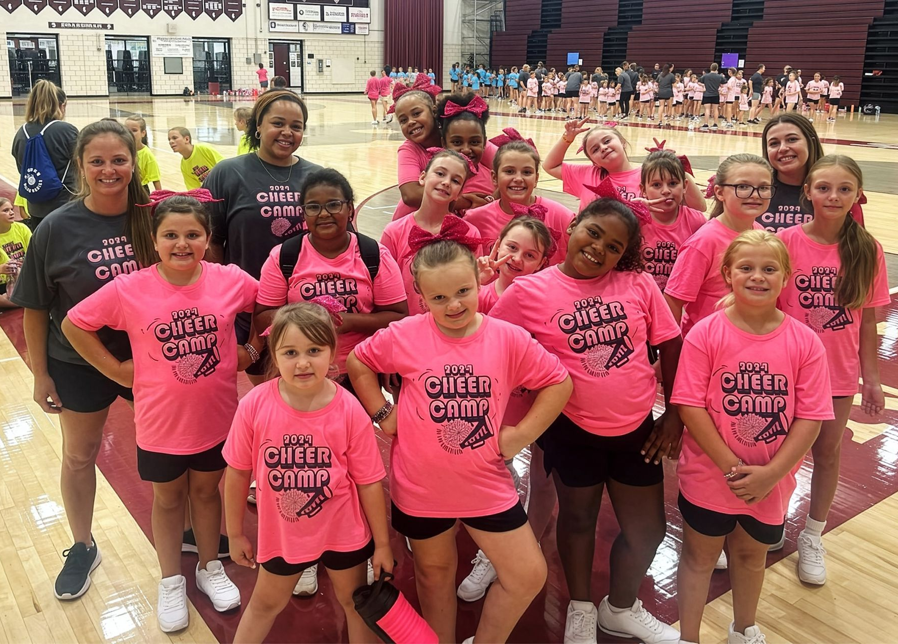Group of people in bright pink shirts posing in a gymnasium during a basketball event