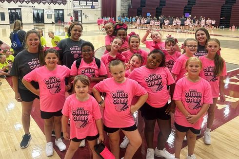 Group of people in bright pink shirts posing together in a gymnasium.