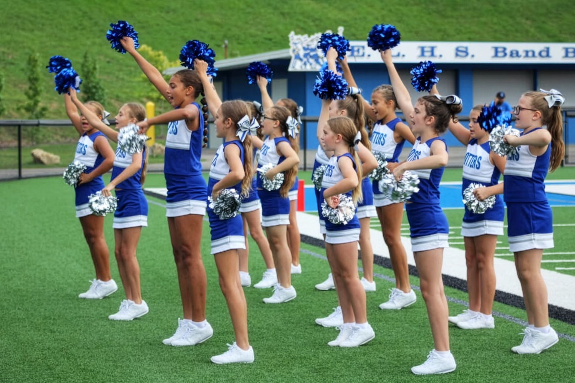 Cheerleaders in blue-and-white uniforms line up on a track holding pom-poms and smiling