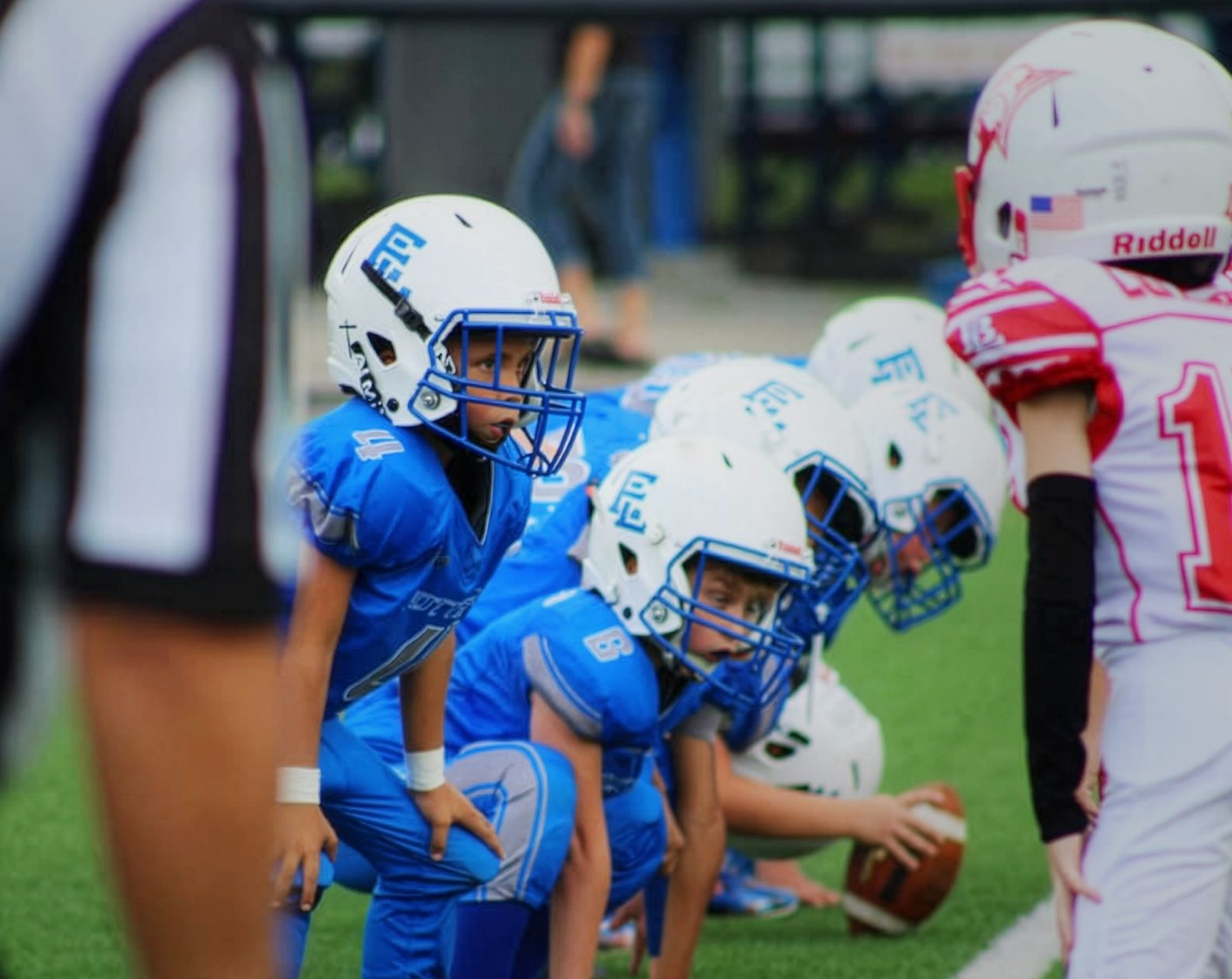 Youth football players in blue crouch at the line against opponents in white and red