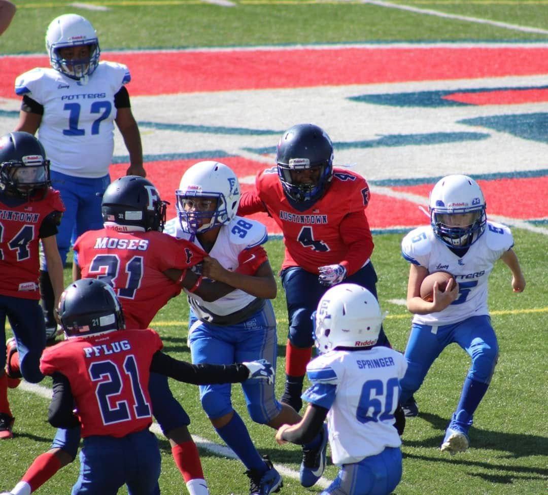 Youth football players in red and white uniforms running on a field during a game