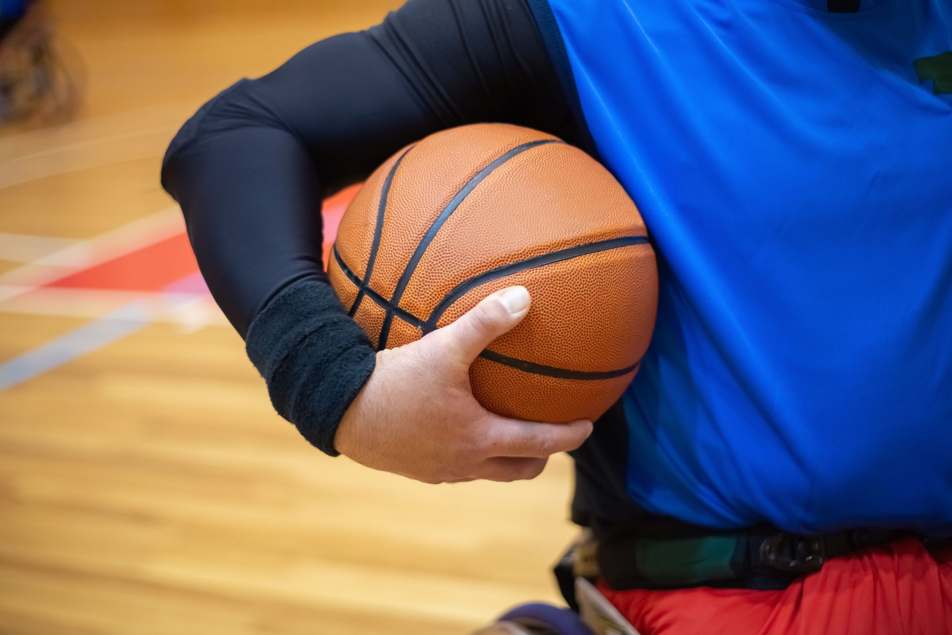 Person holding a basketball in a gym, wearing a blue shirt and black arm sleeve.