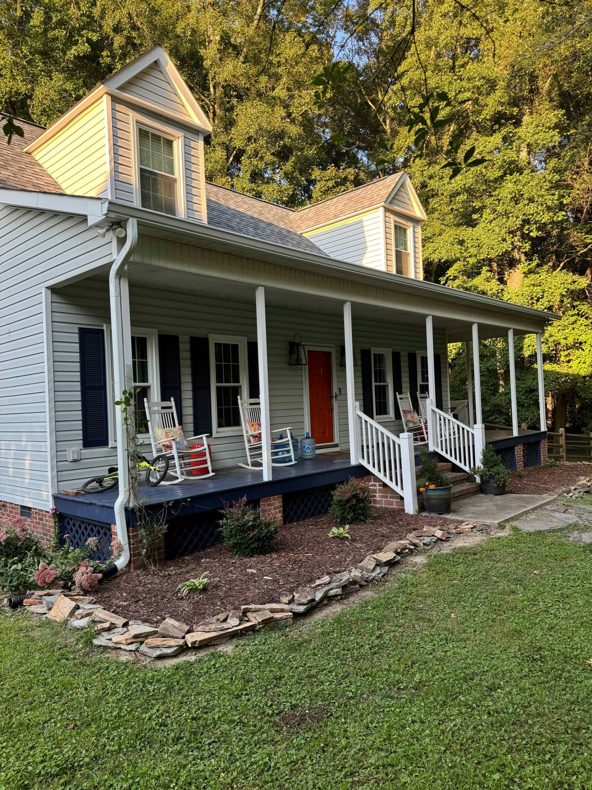 A white house with a large porch and rocking chairs on it.