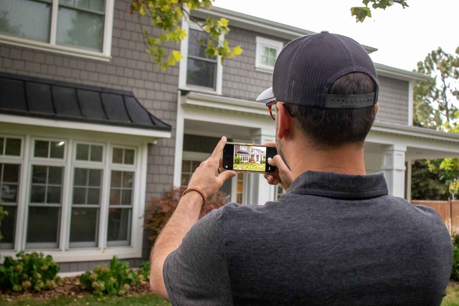 A man is taking a picture of a house with a cell phone.