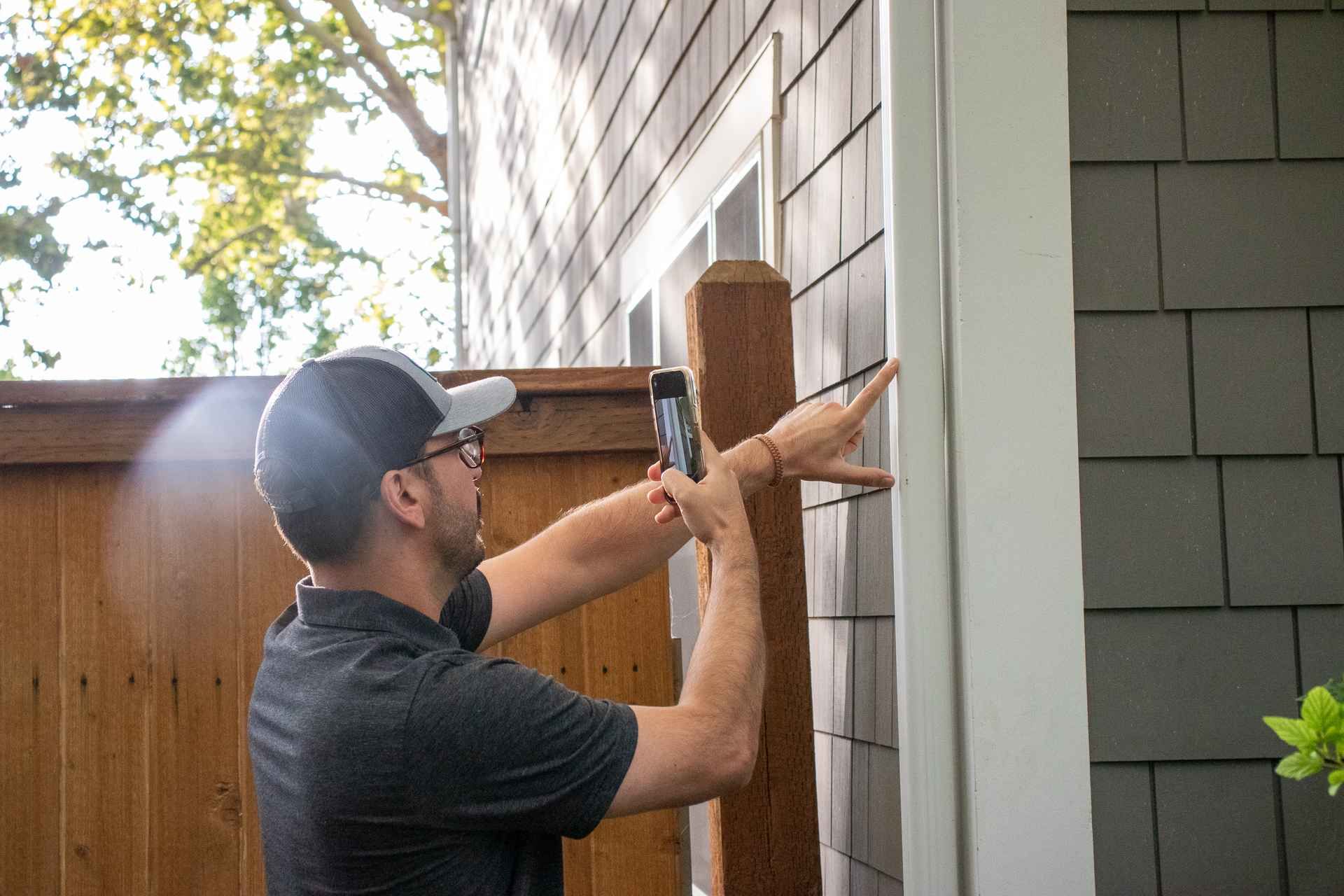 A man is taking a picture of a house with a cell phone.