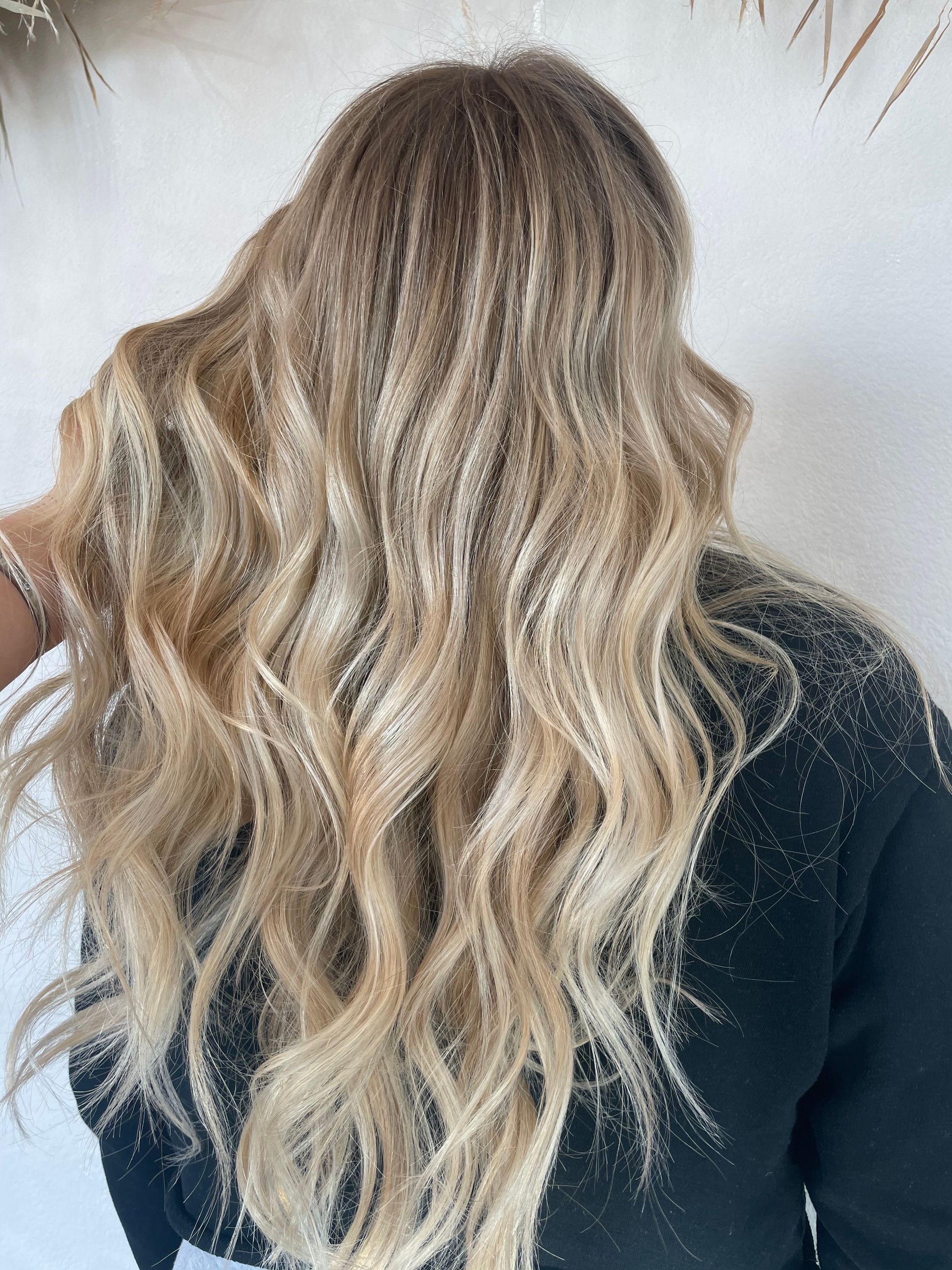 Back view of long wavy blonde hair over a dark top against a light wall