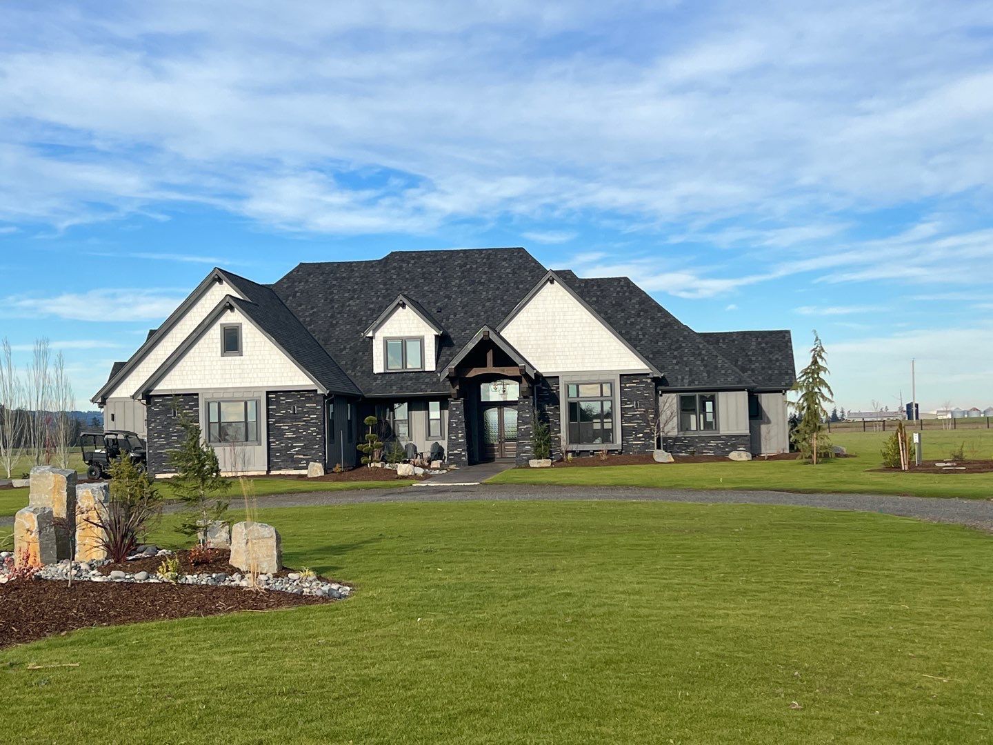 Large modern house with a dark roof, stone accents, and a wide green lawn under a blue sky