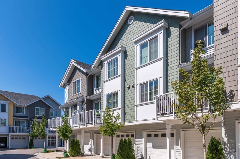 Row of modern townhouse apartments with white balconies and gray siding under a bright blue sky