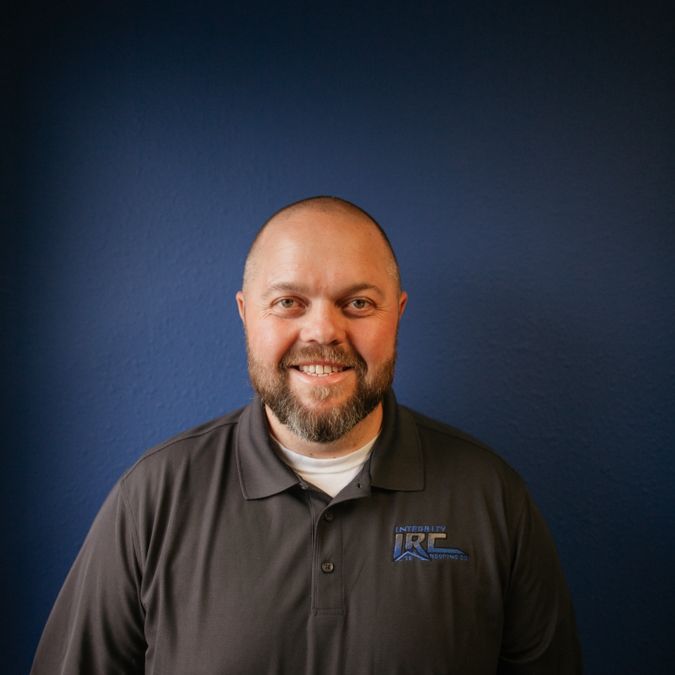 Smiling bald man with beard in dark polo shirt against a blue wall