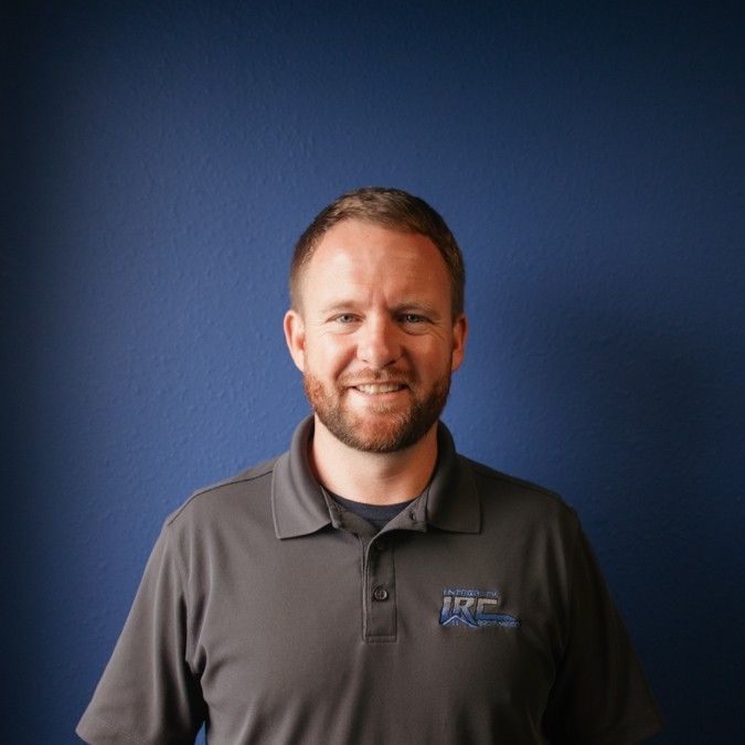 Smiling man in a gray polo shirt standing against a dark blue backdrop