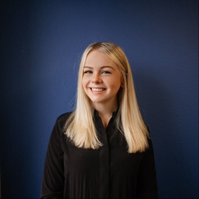 Smiling blonde person in black shirt against a dark blue background