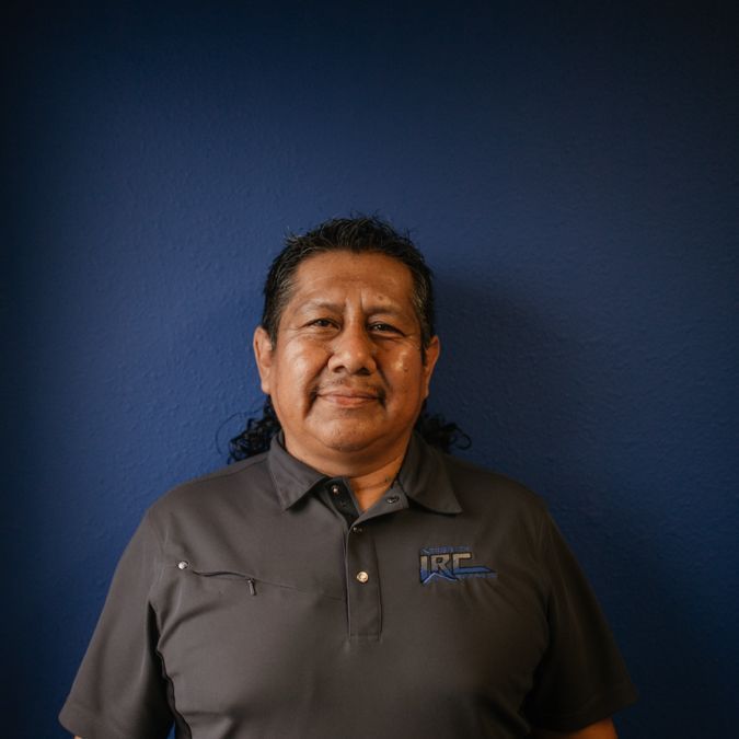 Man standing against a blue backdrop, wearing a gray polo shirt and smiling gently