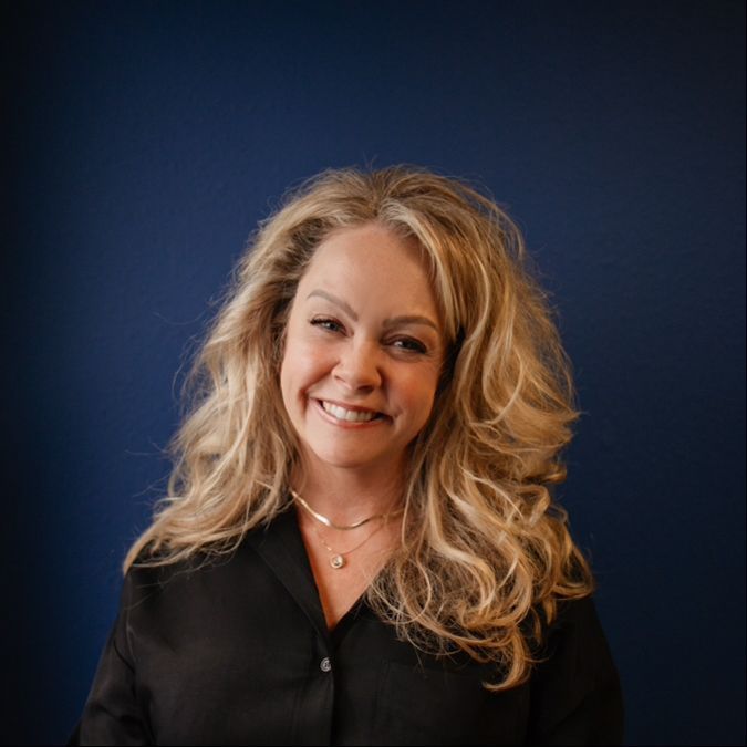 Smiling blonde woman in black blouse against a dark blue background