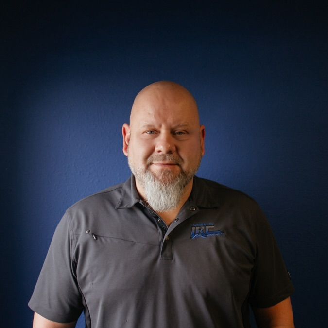 Portrait of a bald man with a gray beard in a dark polo shirt against a blue background