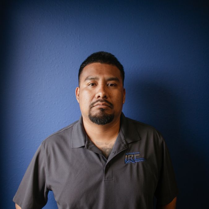 Man standing against a blue wall, wearing a gray polo shirt, looking at the camera.