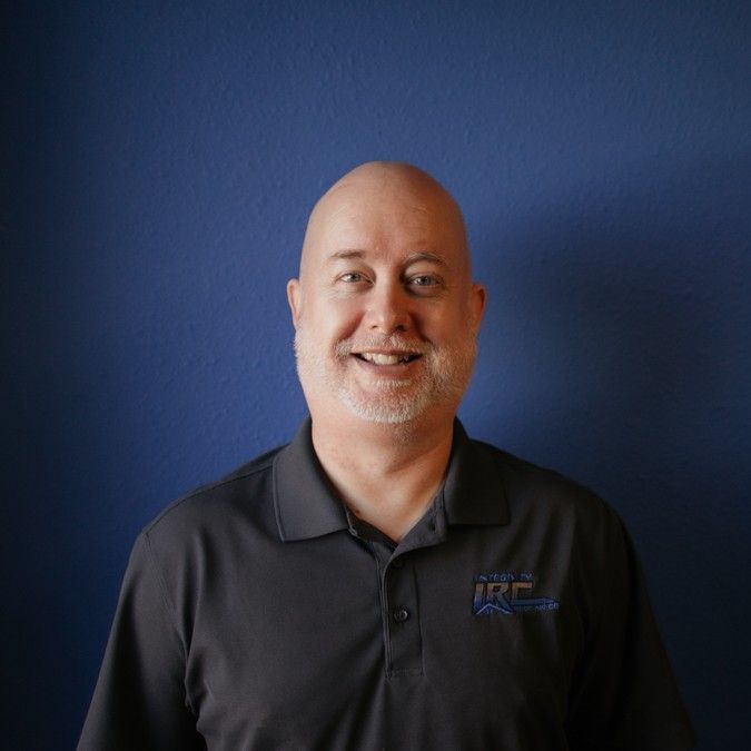 Smiling bald man in a black polo shirt against a blue background