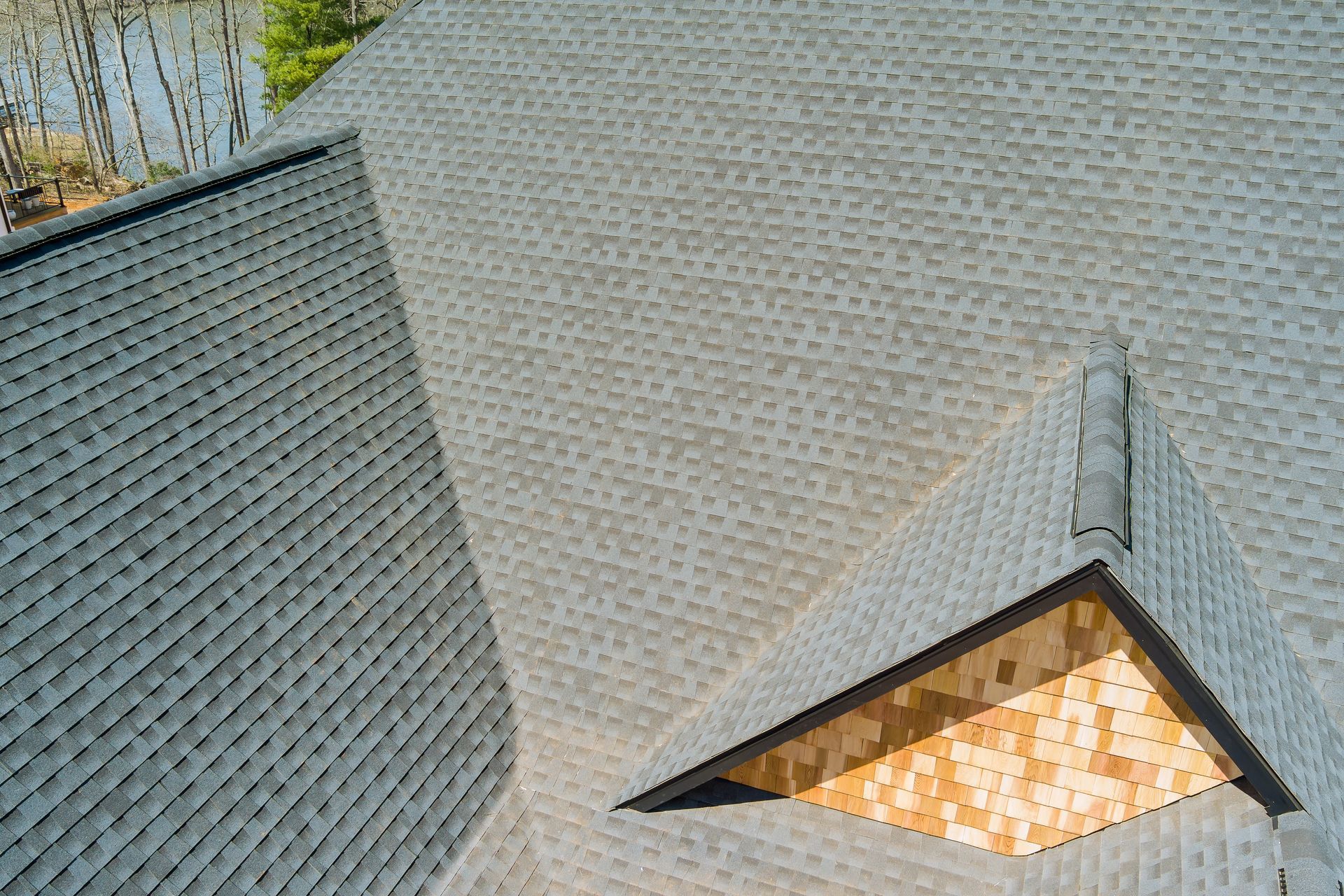 Close-up of a shingled roof with a small triangular dormer window glowing warm light.